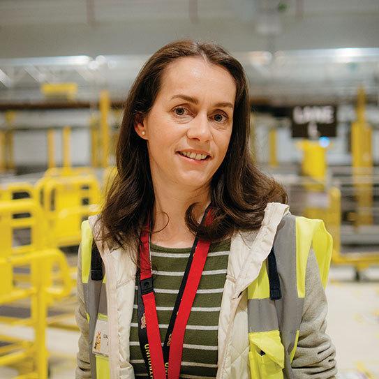 Female with brown hair, in high vis jacket, smiling at the camera.