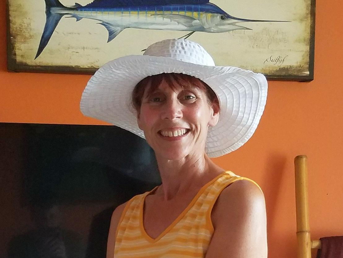 A photo of AWS builder Suzanne Nickson wearing a white hat in front of an orange wall with a piece of hanging art.