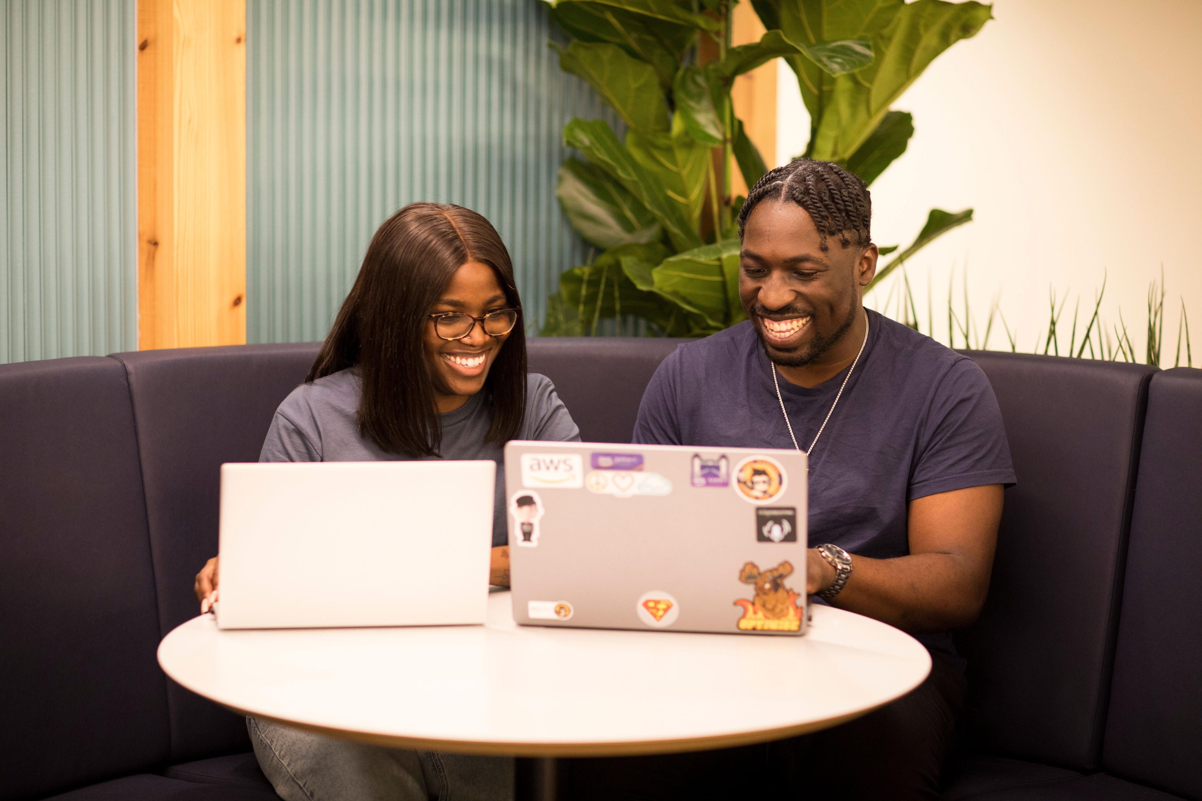 A man and woman smiling looking at their computers.