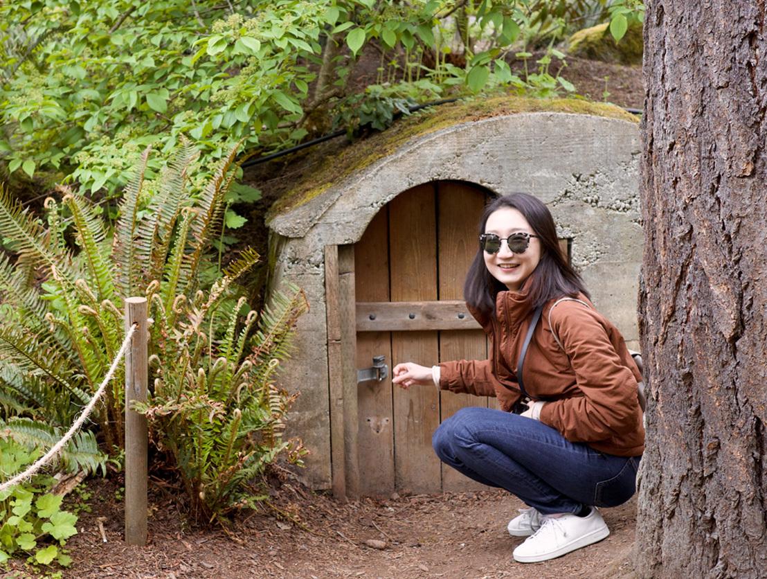 Firmware Engineer Yuhui Zheng poses in front of a small doorway in the woods, wearing sunglasses and smiling.