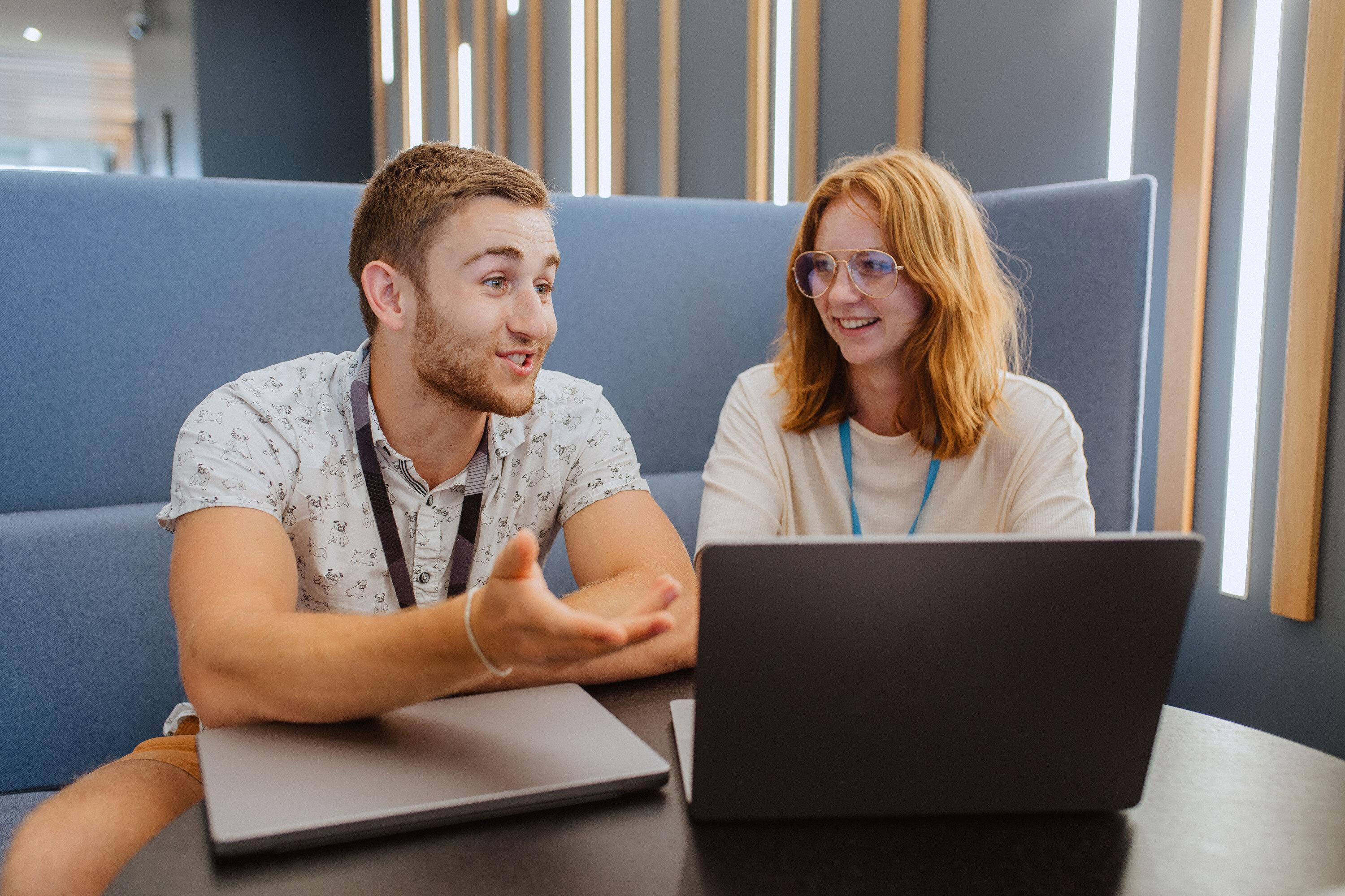 A man with his hand extended towards a laptop screen a woman with glasses listening