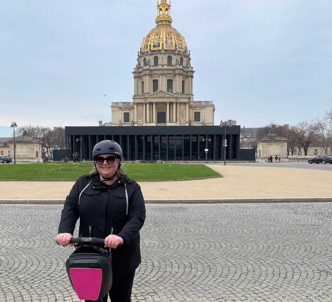 Photo of Kathy, an AWS builder working in generative AI, riding a scooter in front of an ornate building.